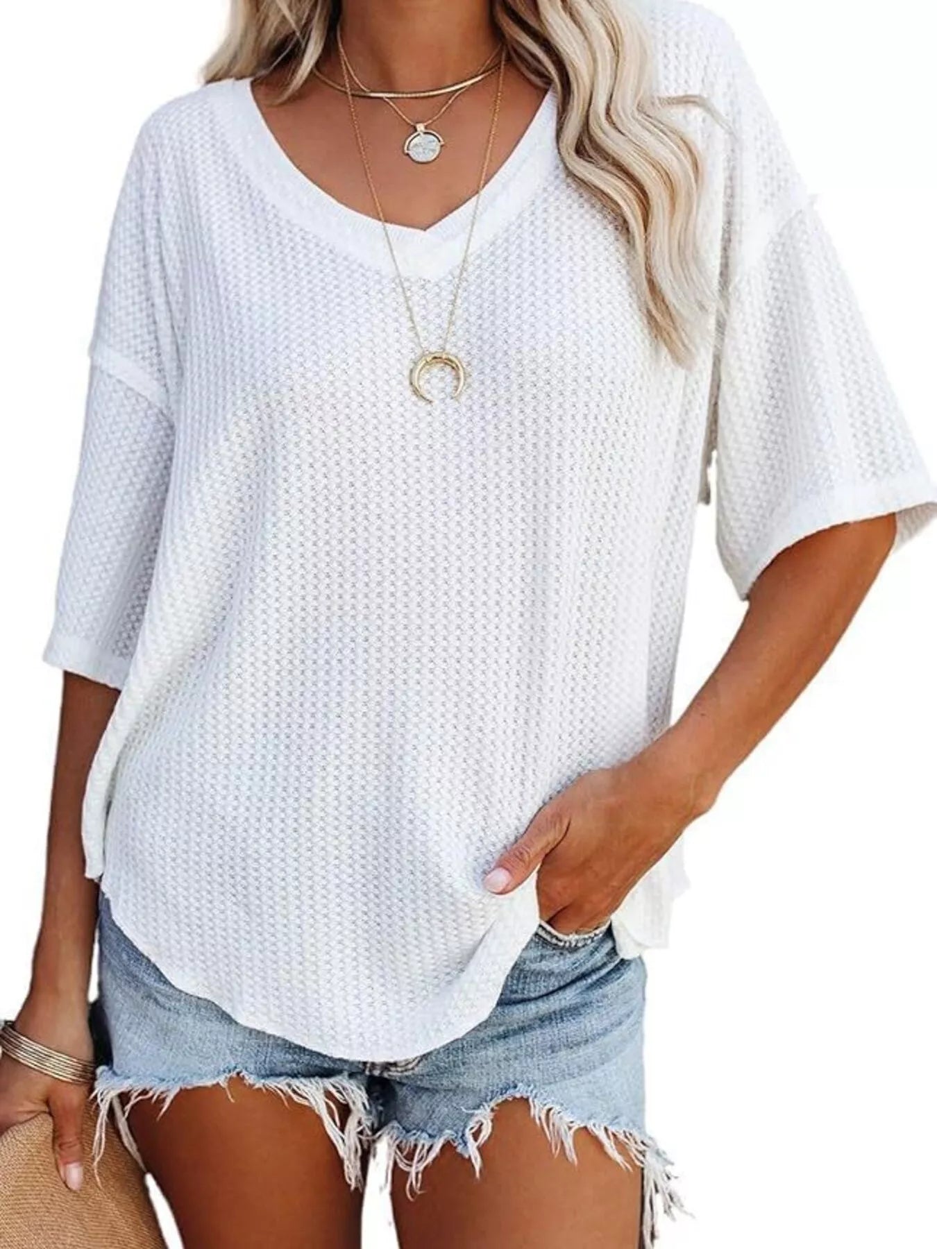 Woman wearing a white textured top and denim shorts with a plain background
