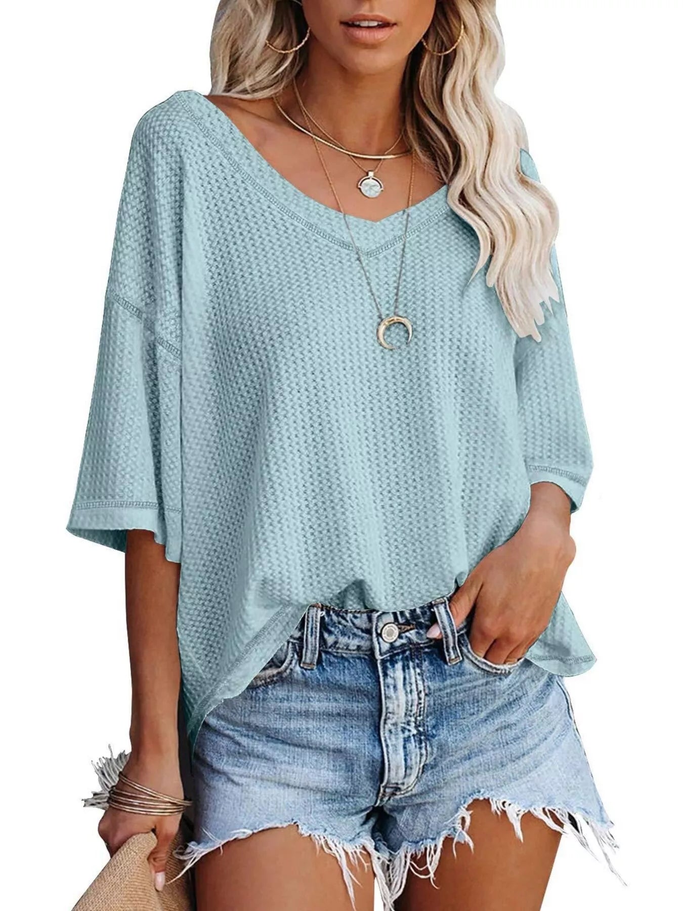 Woman wearing a light blue textured top and denim shorts on a white background
