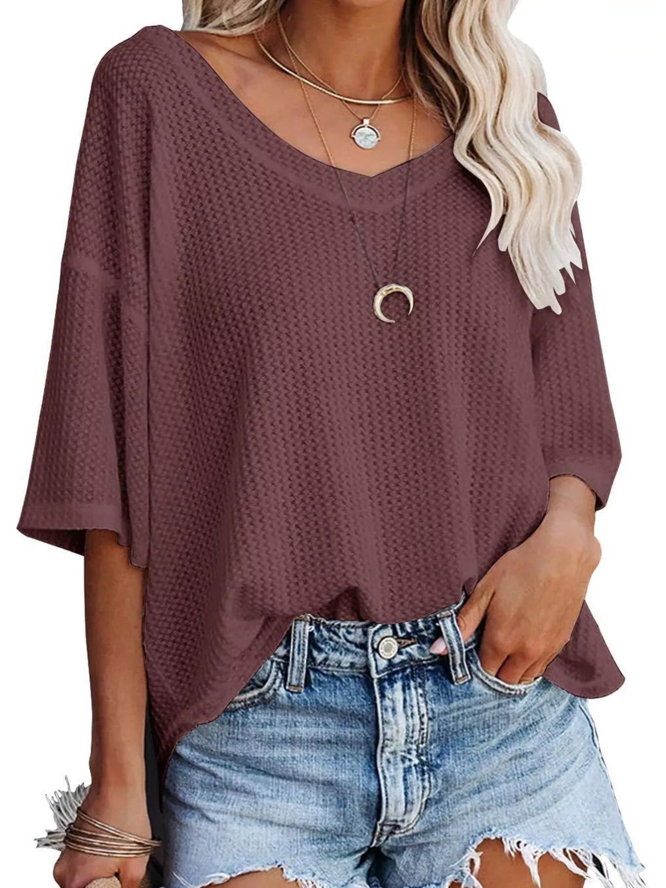 Woman wearing a loose-fitting purple top and denim shorts on a white background