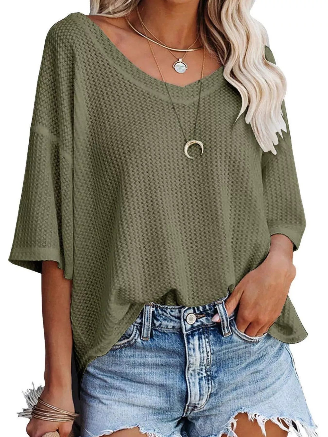 Person wearing an olive green textured top and denim shorts on a white background