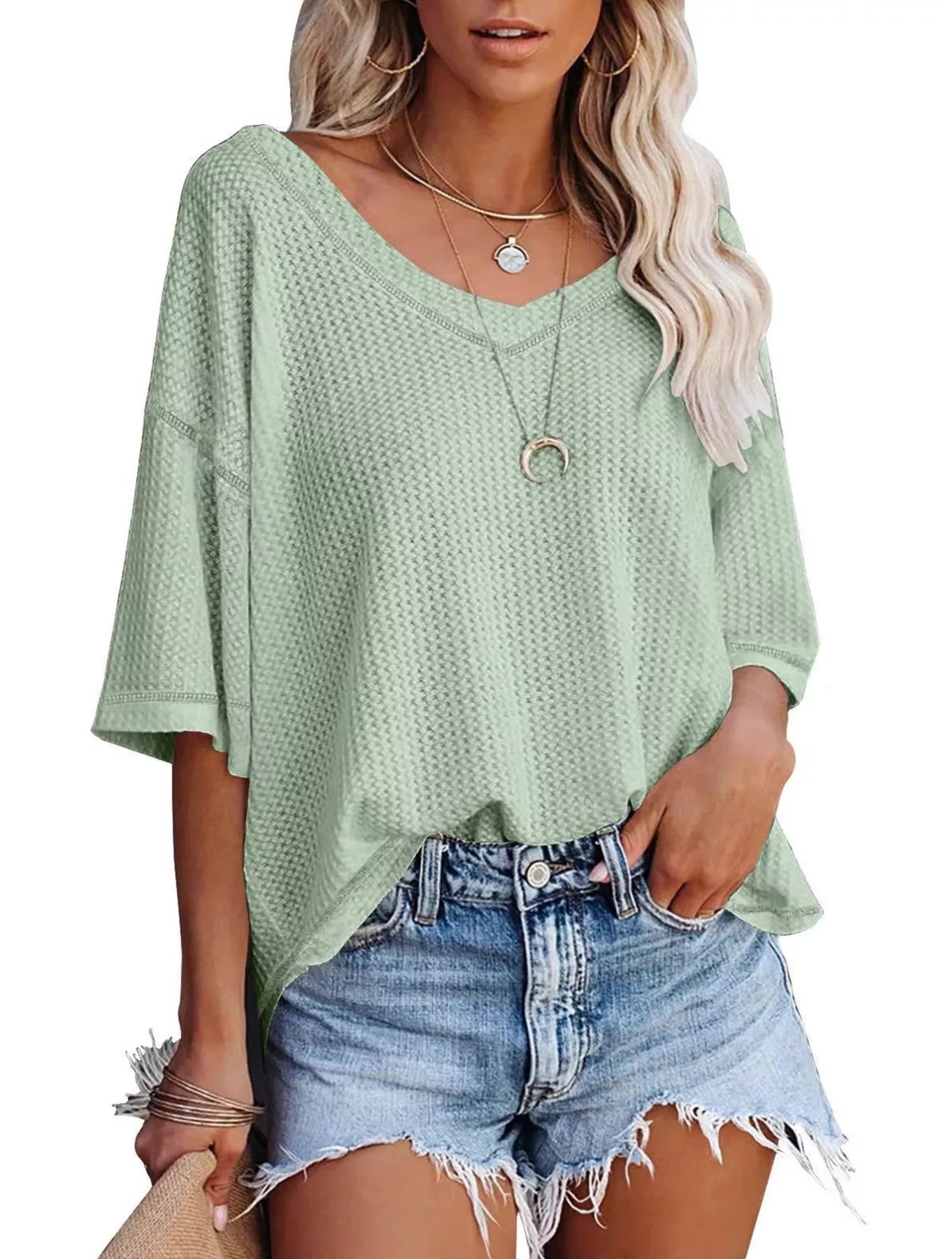 Woman wearing a light green textured top and denim shorts on a white background