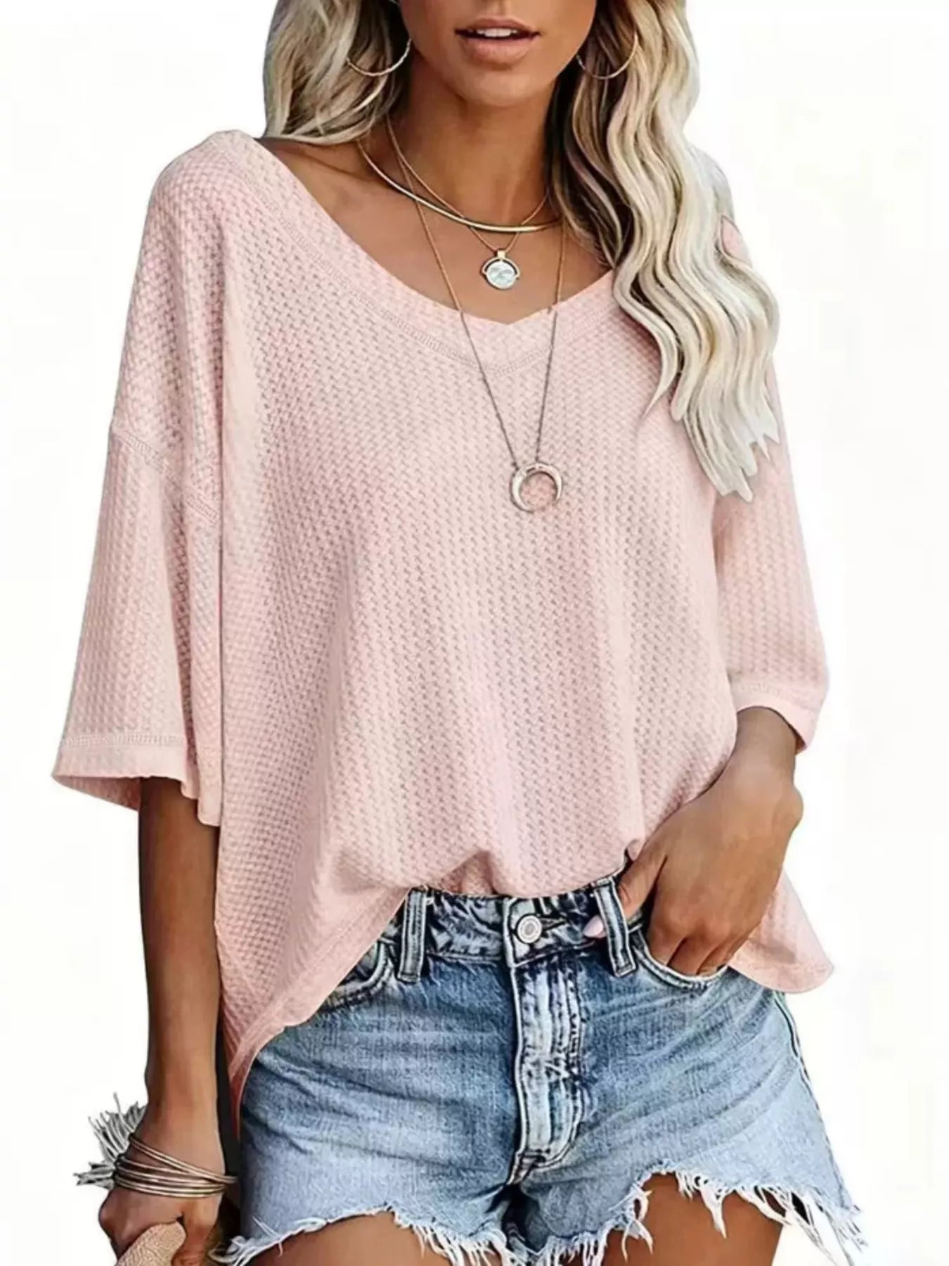 Woman wearing a pink oversized top and denim shorts on a white background