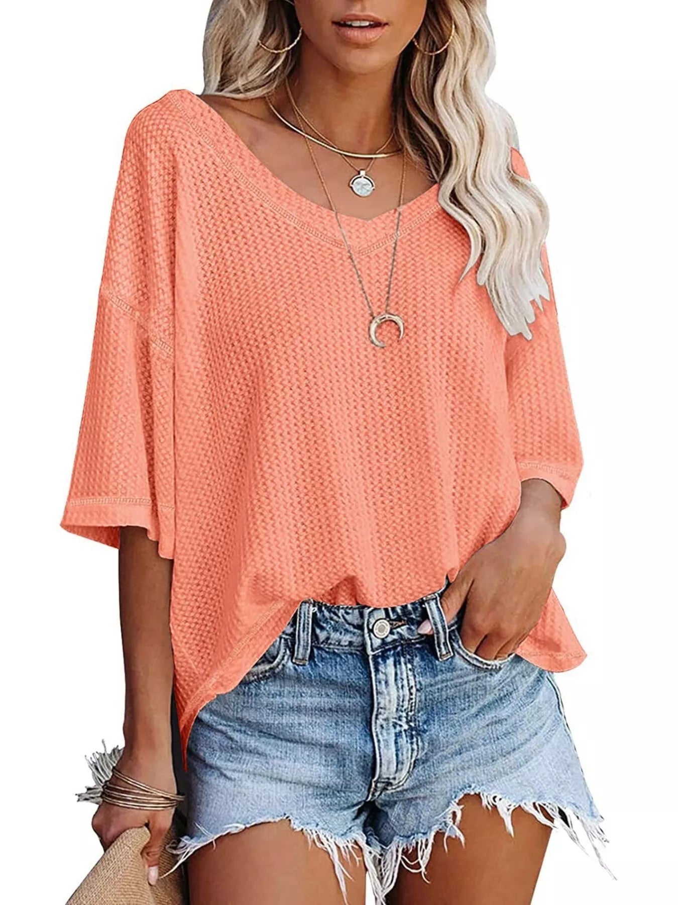 Woman wearing a coral top and denim shorts on a white background