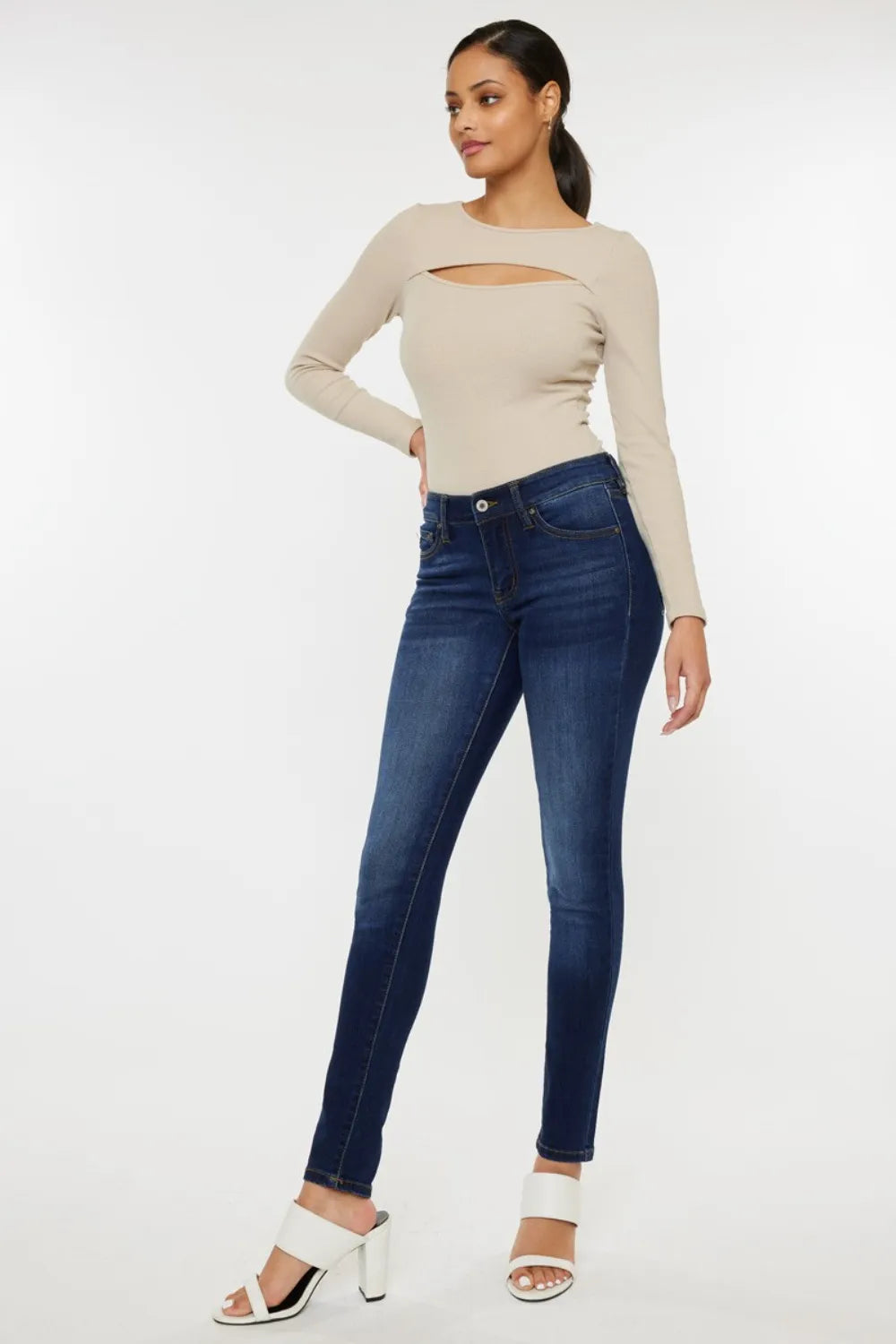 Woman wearing a beige long-sleeve top and blue jeans on a white background