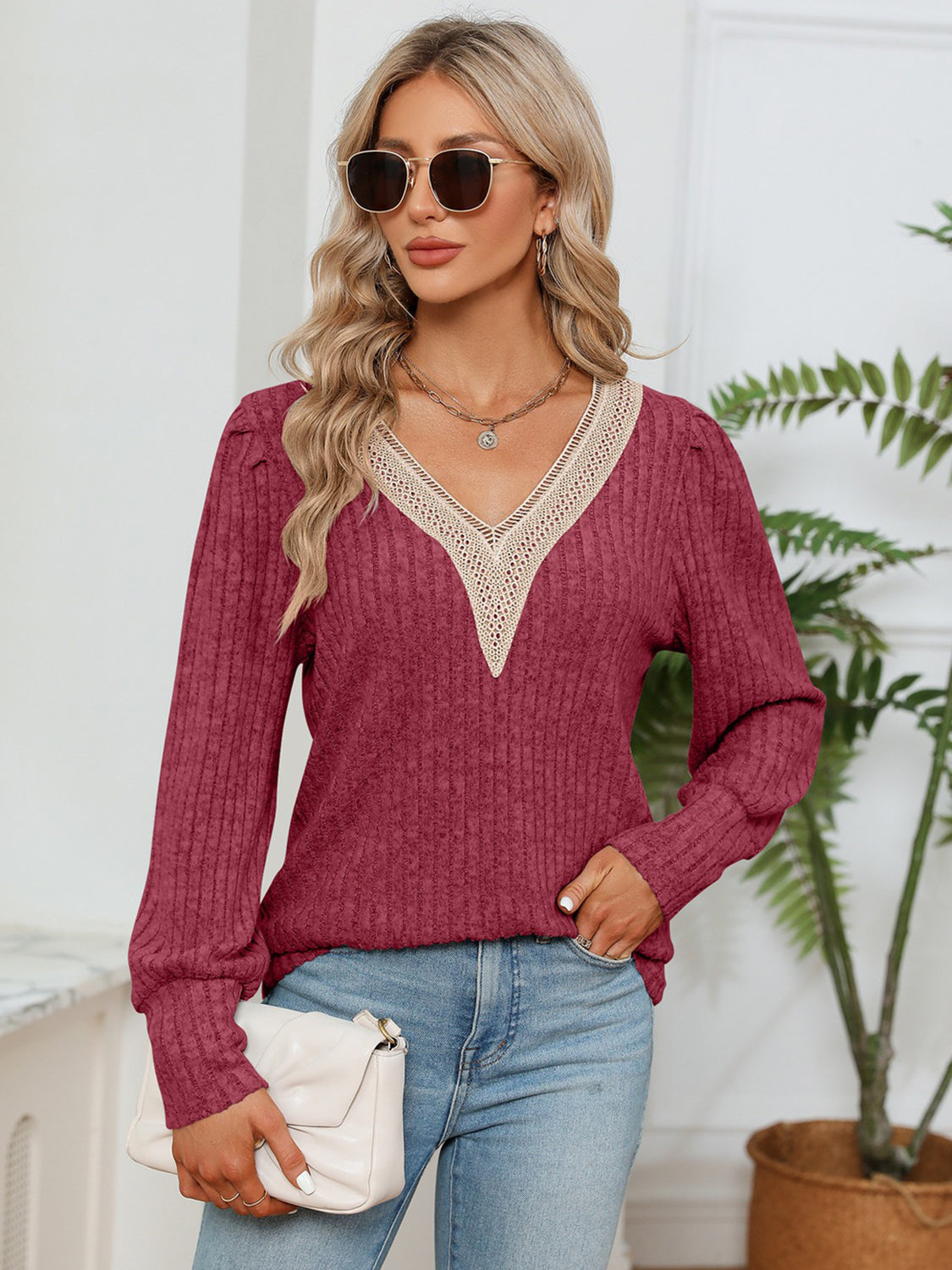 Woman wearing a burgundy sweater with lace details and blue jeans, holding a white clutch.