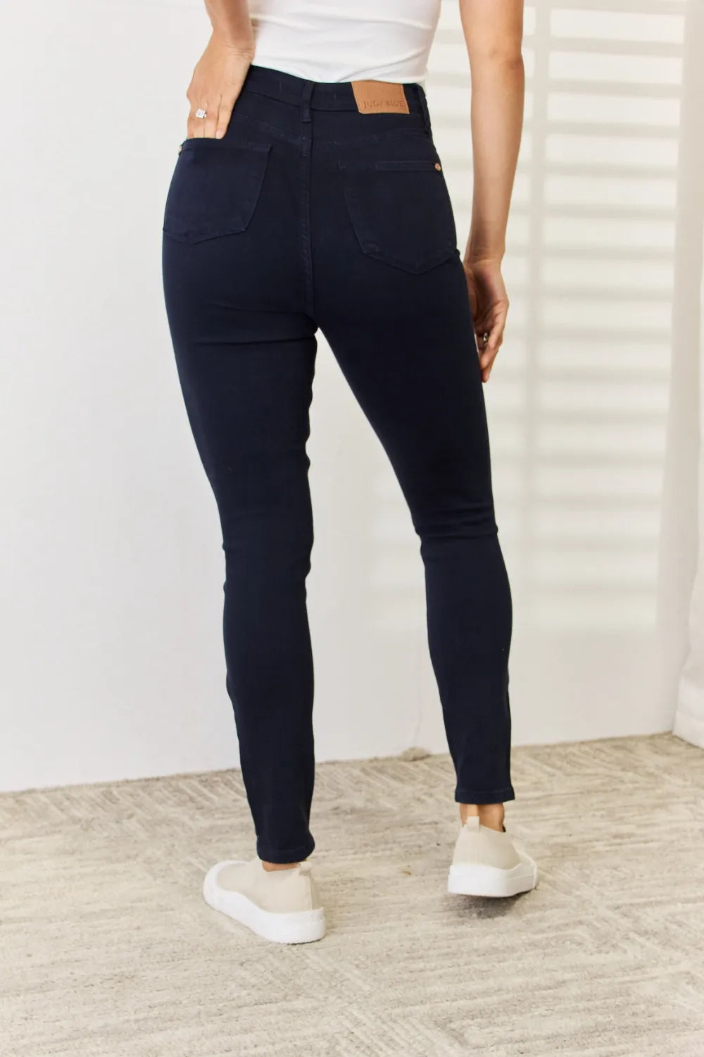 Person wearing navy blue pants and white sneakers in a minimal indoor setting