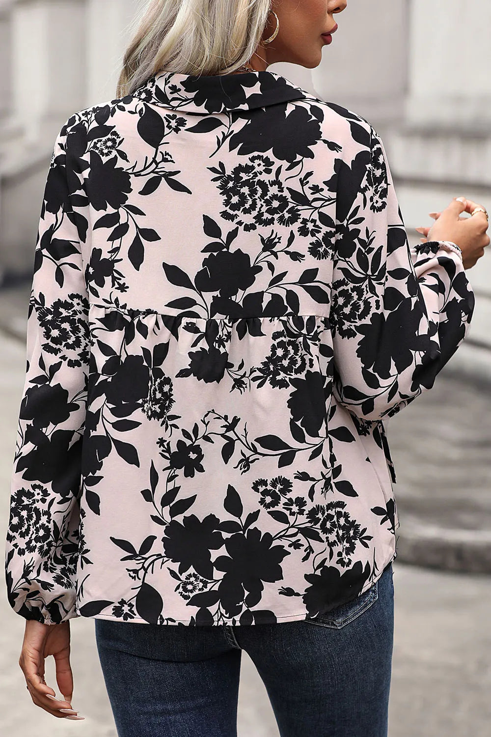 Person wearing a floral patterned blouse with black flowers on a light pink background.