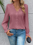 Woman wearing a pink blouse and blue jeans, holding a black cup against a gray wall.