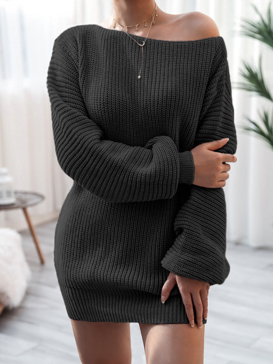 Person wearing a black ribbed sweater dress in a minimalistic room.