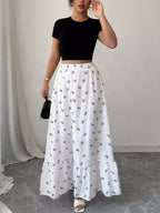 Woman wearing a black crop top and white skirt with butterfly pattern indoors.