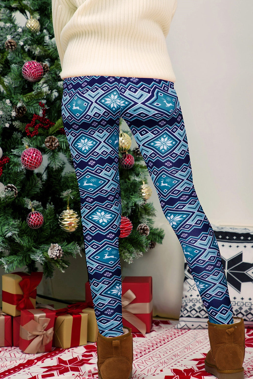 Person wearing blue patterned leggings standing in front of a decorated Christmas tree with presents.