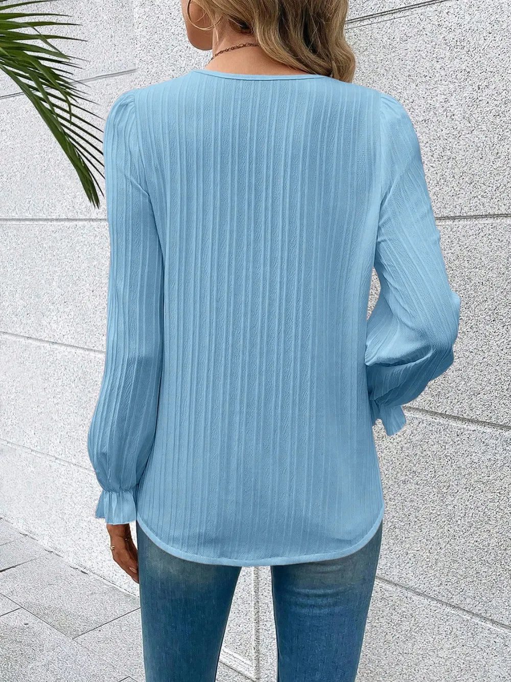 Person wearing a light blue blouse with long sleeves against a light gray wall.