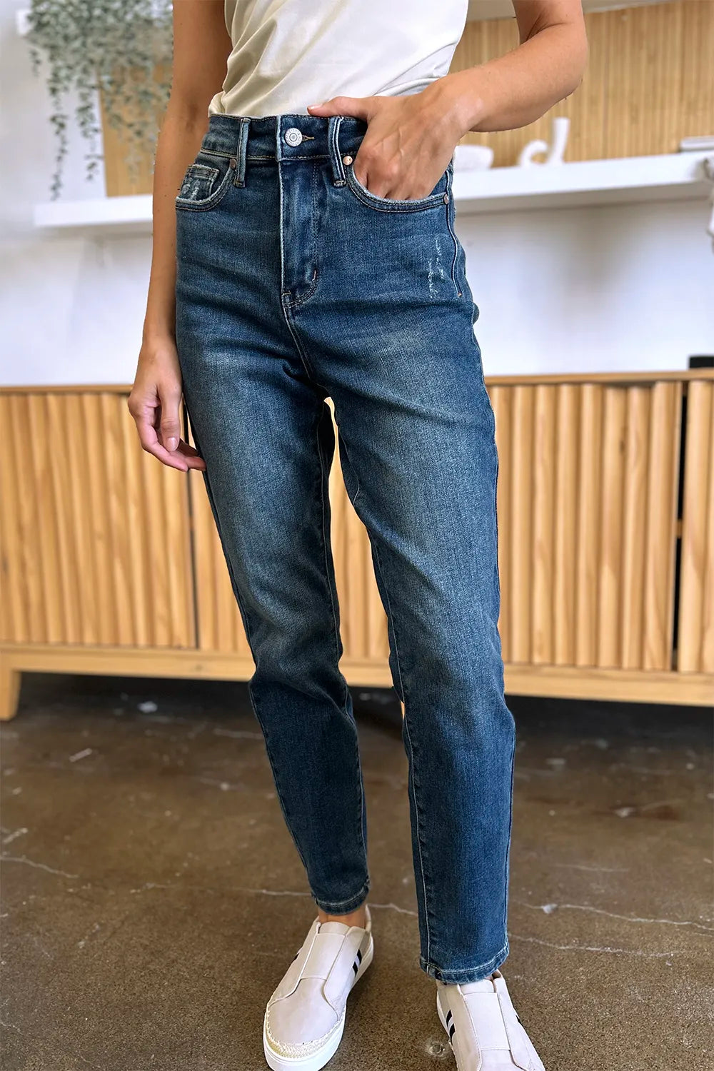 Person wearing blue jeans and white sneakers in an indoor setting