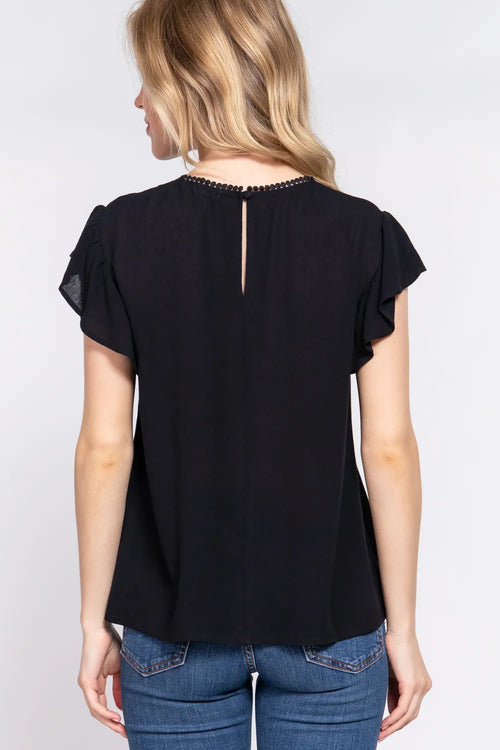 Woman wearing a black top with sheer sleeves and blue jeans on a white background