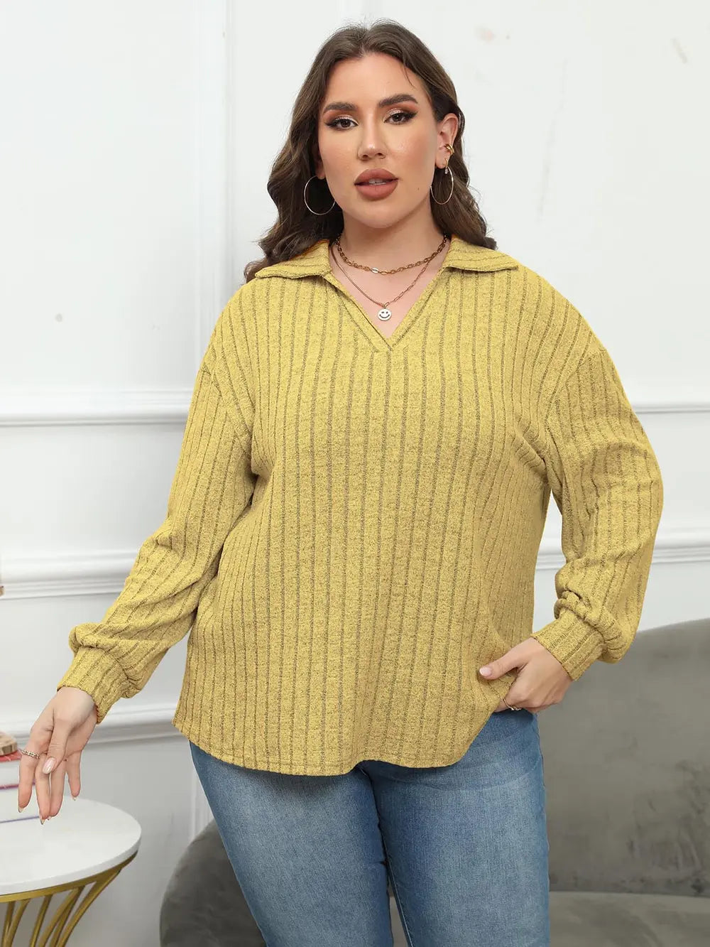 Woman wearing a yellow ribbed sweater and blue jeans indoors.