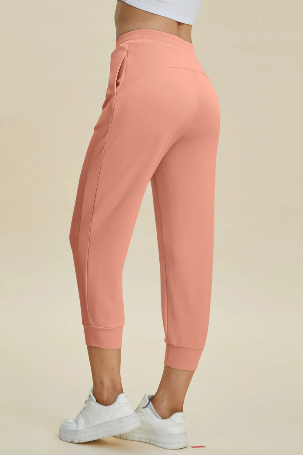 Coral jogger pants worn by a person on a beige background