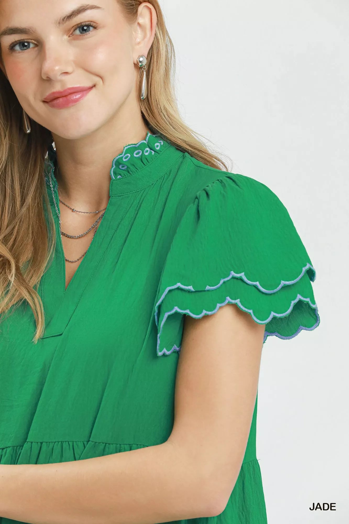 Woman wearing a green dress with scalloped sleeves on a white background