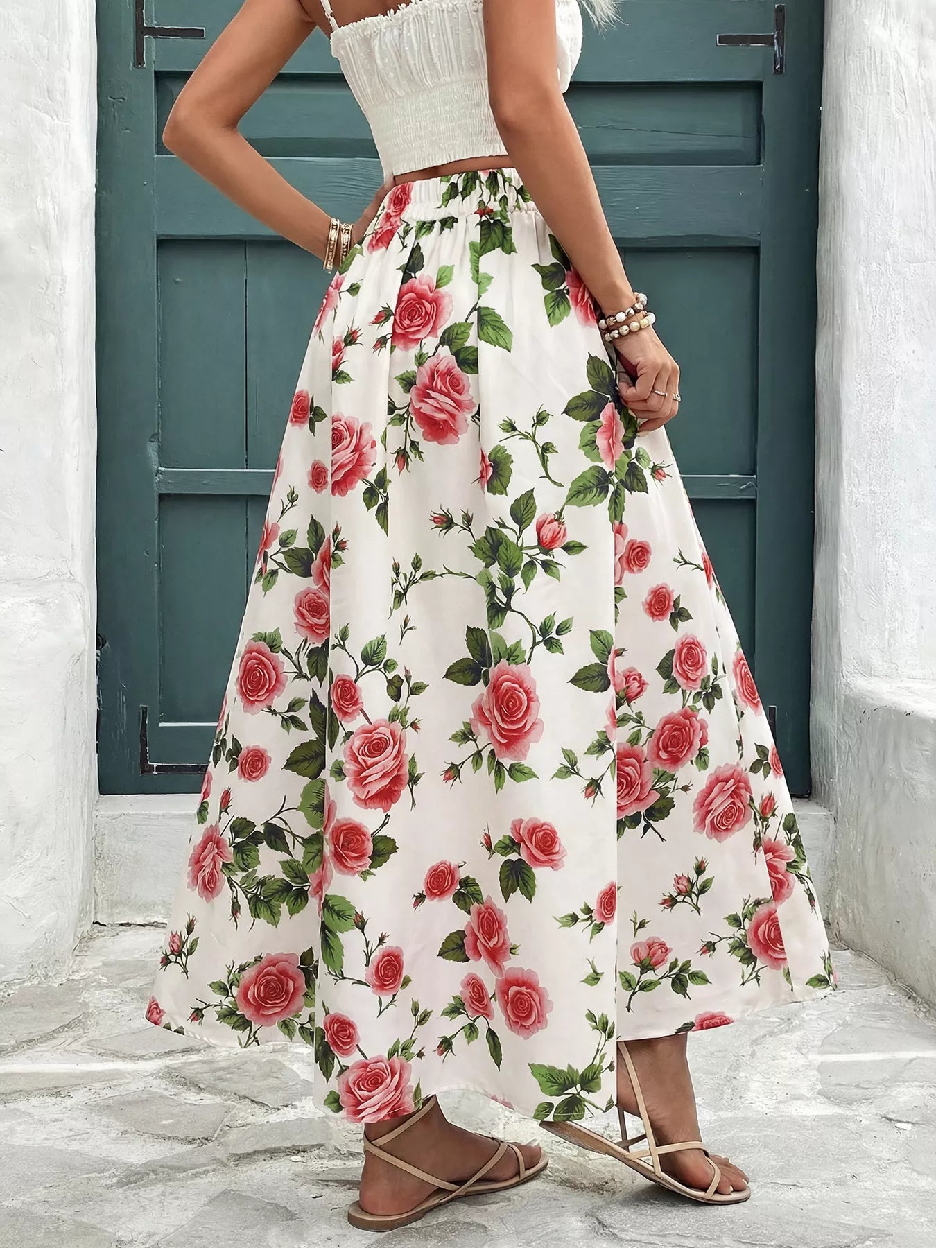 Person wearing a white top and floral skirt with red roses in front of a blue door.