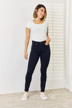 Woman wearing a white t-shirt and dark blue jeans standing against a white wall.