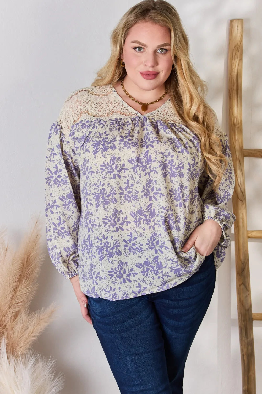 Woman wearing a floral blouse and dark pants against a white background