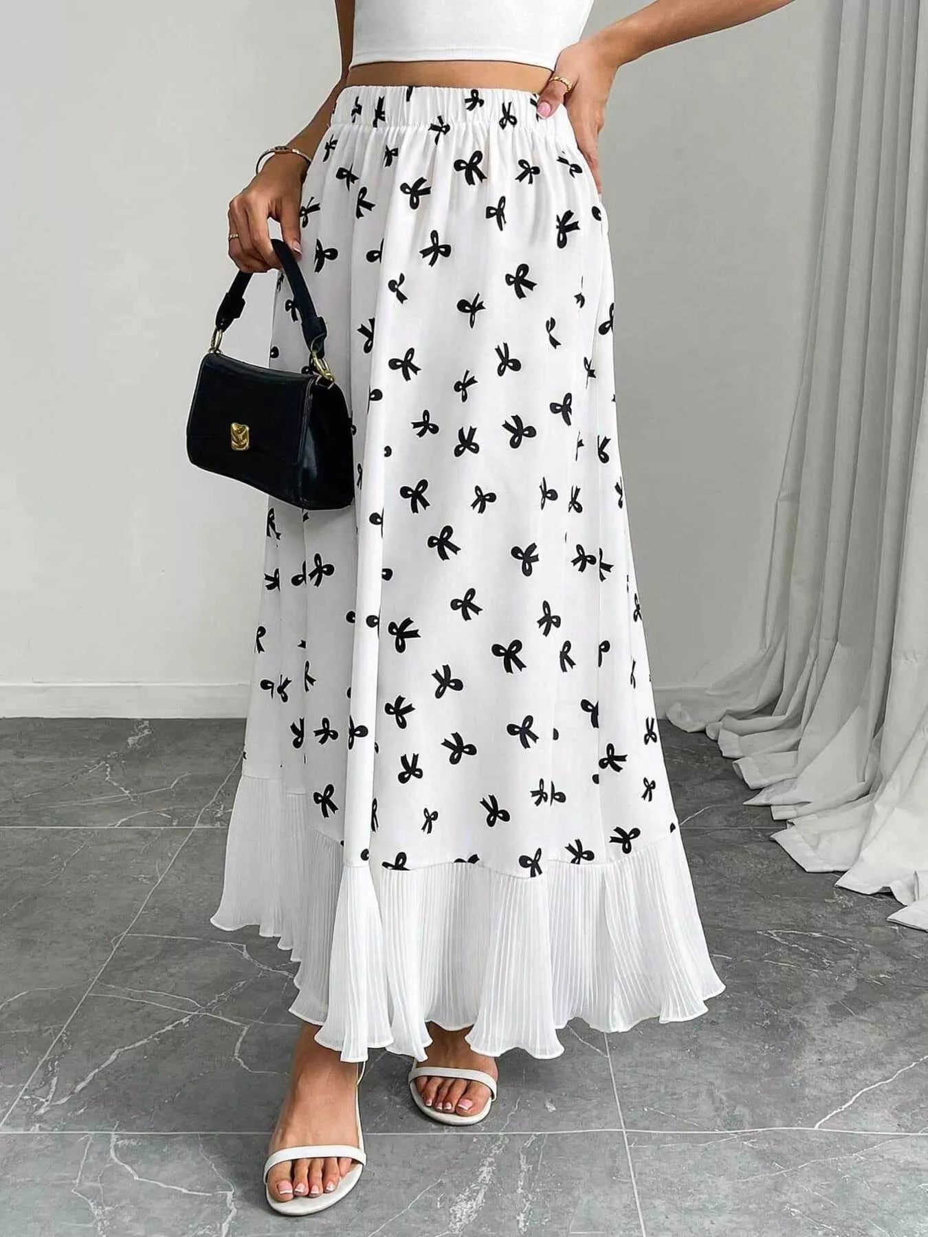Woman wearing a white dress with black floral patterns, holding a black handbag indoors.