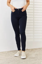 Person wearing dark blue jeans and white sneakers against a white wall.