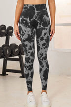 Person wearing gray and black patterned leggings in a gym setting with weights in the background.