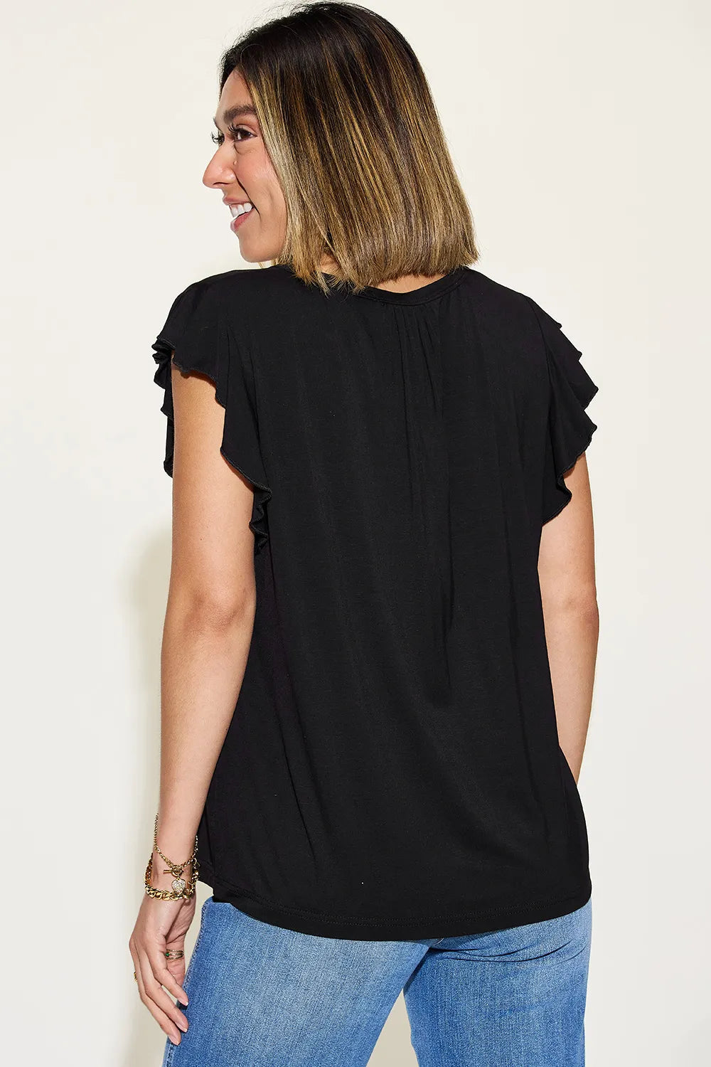 Woman wearing a black top with ruffled sleeves against a white background