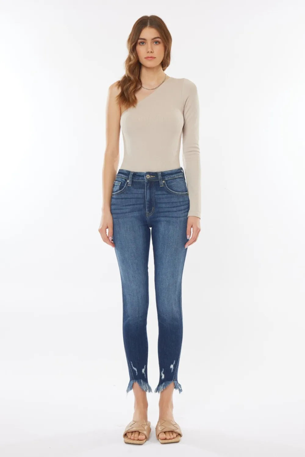 Woman wearing a beige long-sleeve top and blue jeans on a white background