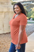 Woman wearing an orange shirt and blue jeans standing outdoors with a blurred background