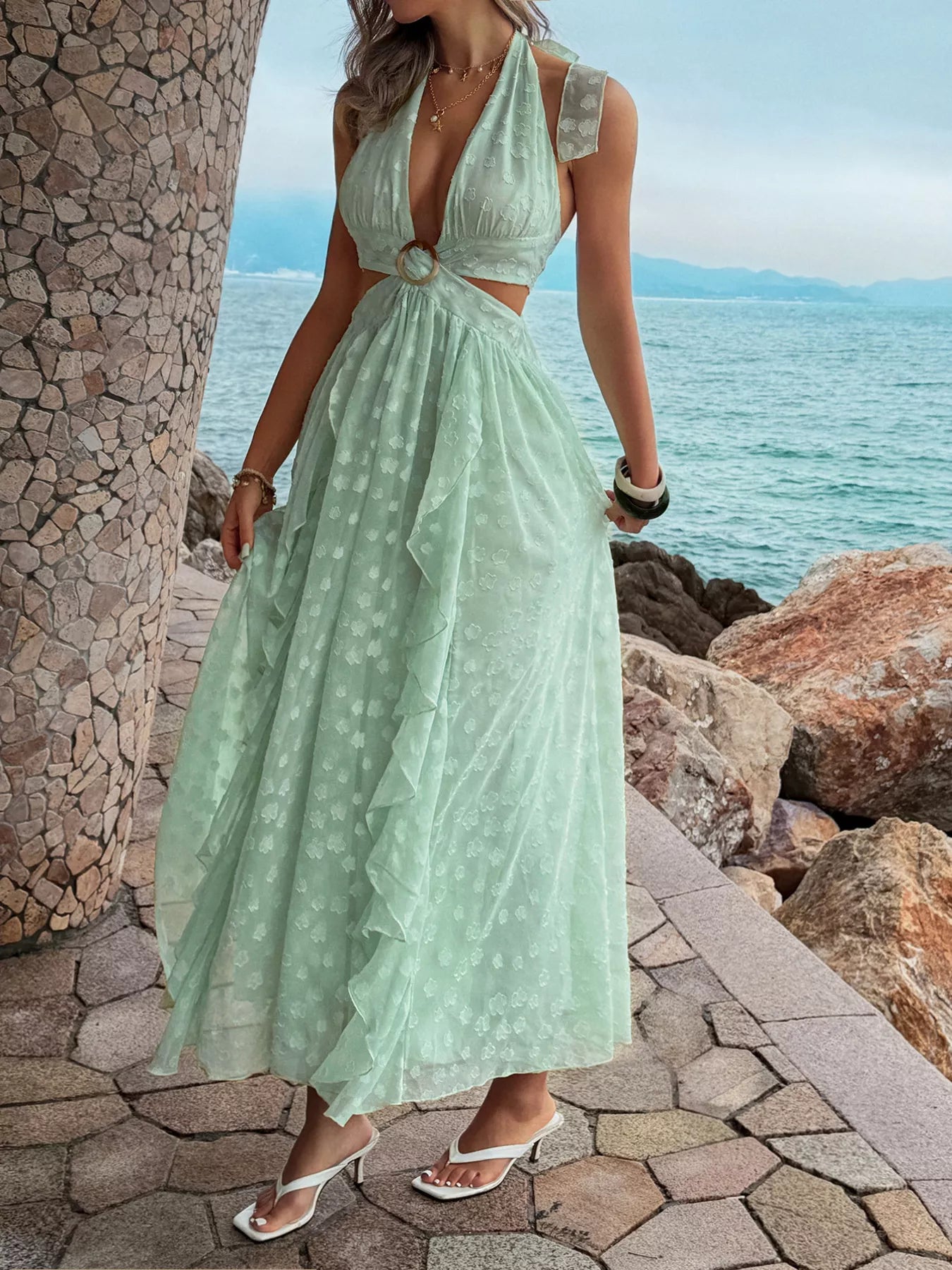 Woman in a light green dress standing by a stone wall with ocean view