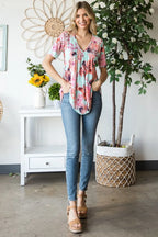 Woman wearing a floral blouse and jeans standing in a room with plants and decor.