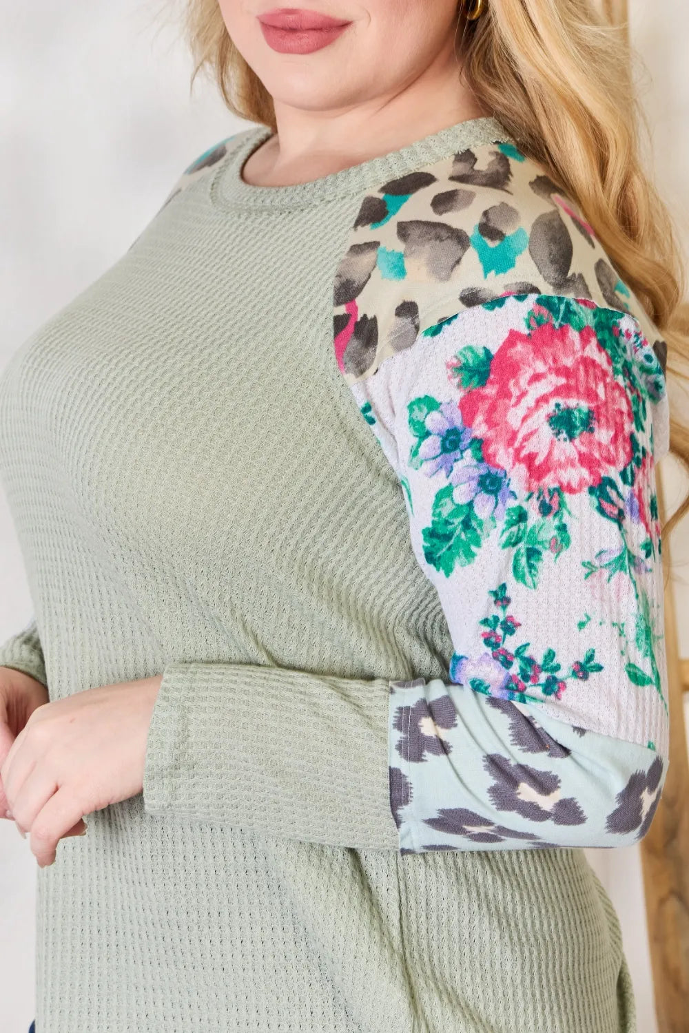 Person wearing a green sweater with a floral and leopard print pattern on the sleeve.