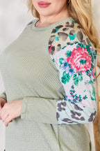 Person wearing a green sweater with a floral and leopard print pattern on the sleeve.