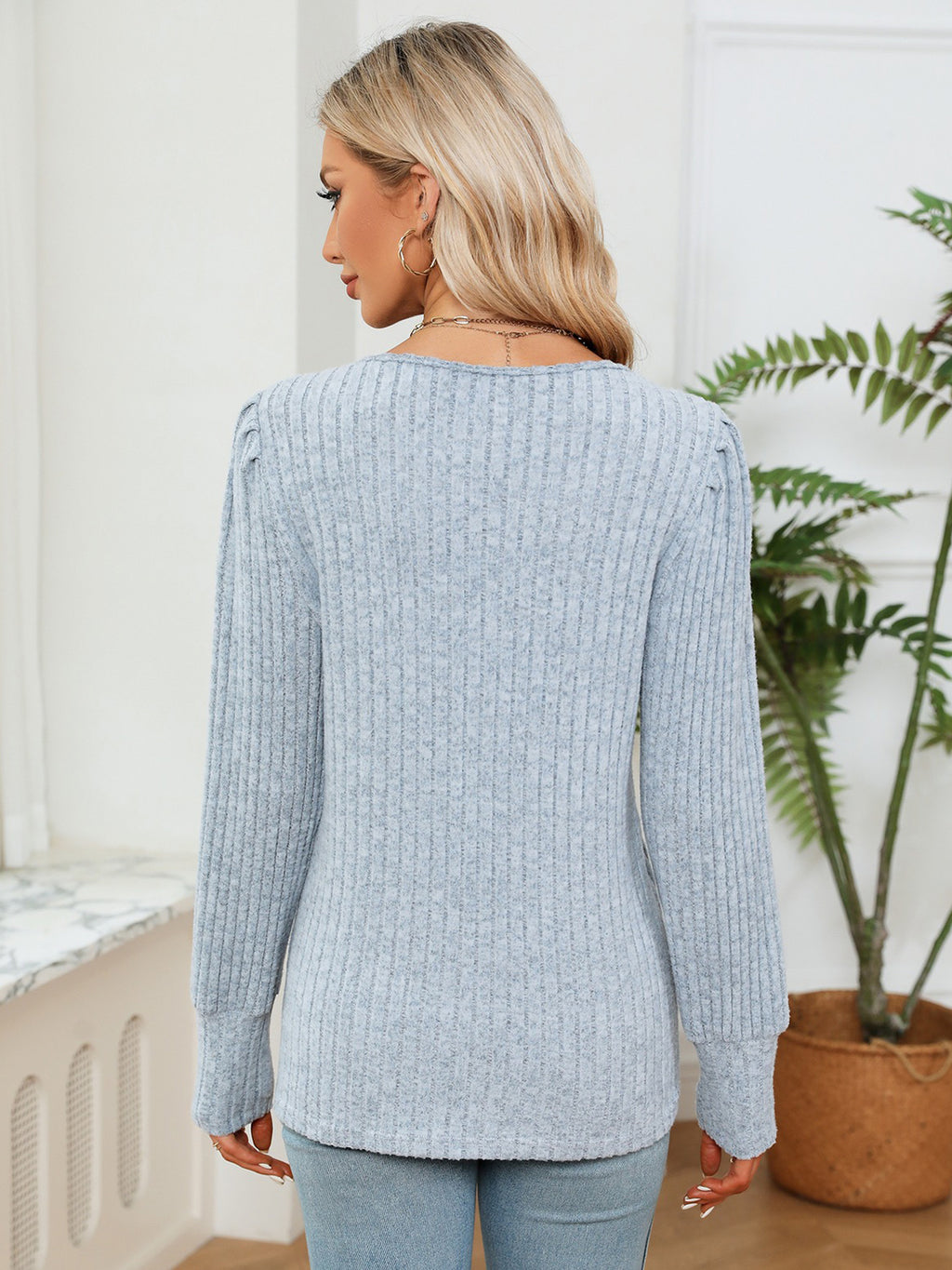 Woman wearing a light blue sweater in a room with a plant