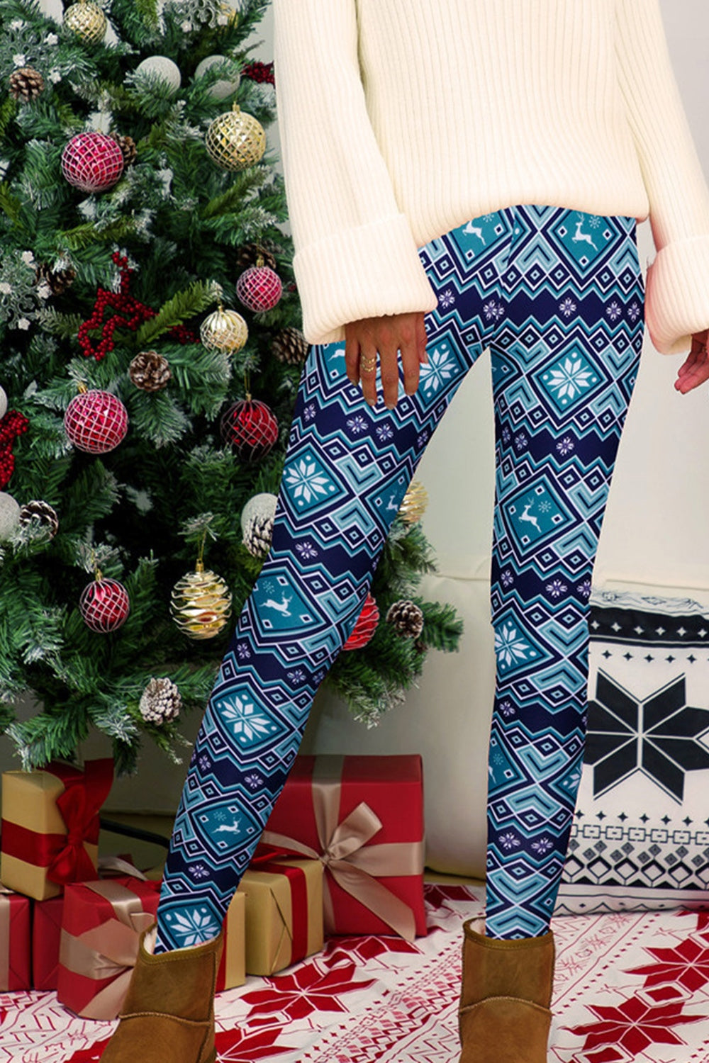 Person wearing blue patterned leggings standing in front of a decorated Christmas tree with presents underneath.