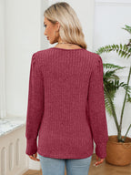 Woman wearing a maroon sweater in a room with a plant and white wall.