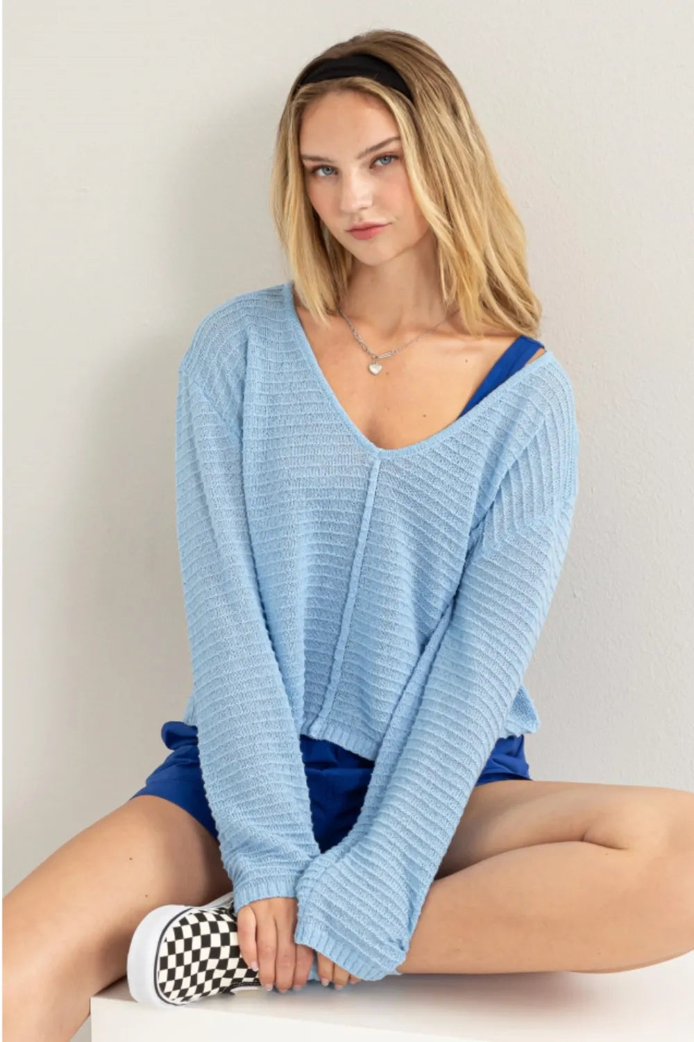 Woman wearing a light blue sweater and blue shorts sitting on a white surface.