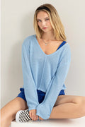 Woman wearing a light blue sweater and blue shorts sitting on a white surface.
