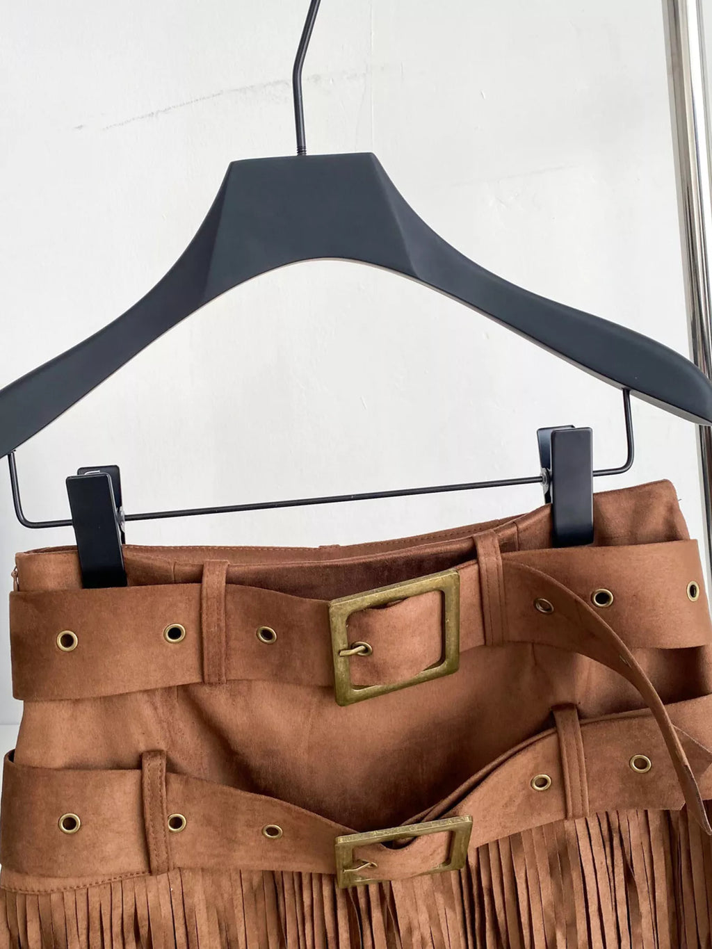 Brown suede skirt with gold buckles on a black hanger against a white background