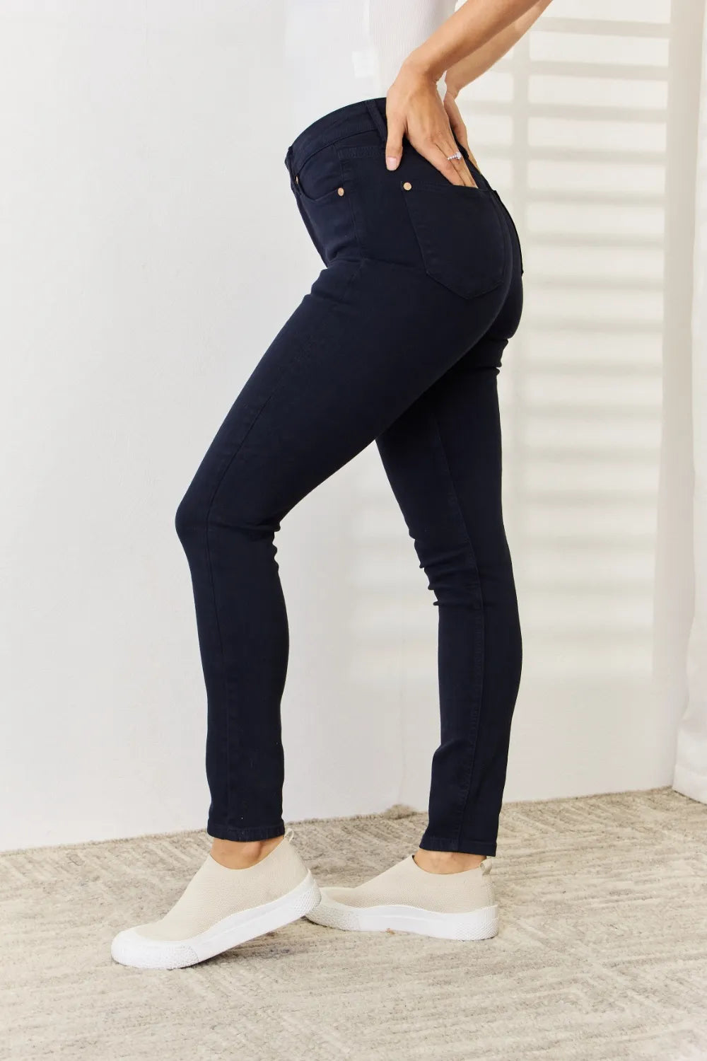 Person wearing navy blue jeans and white sneakers in a minimal indoor setting