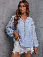 Woman wearing a light blue lace-trimmed blouse against a gray concrete wall.