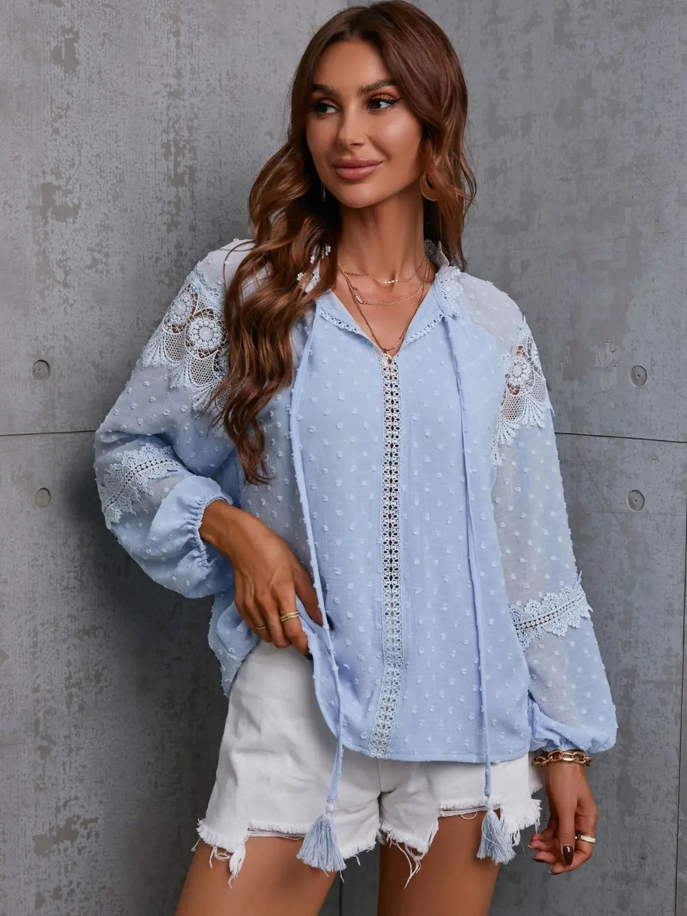 Woman wearing a light blue lace-trimmed blouse against a gray concrete wall.
