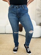 Person wearing blue jeans with slight distressing, standing in a room with a white couch.