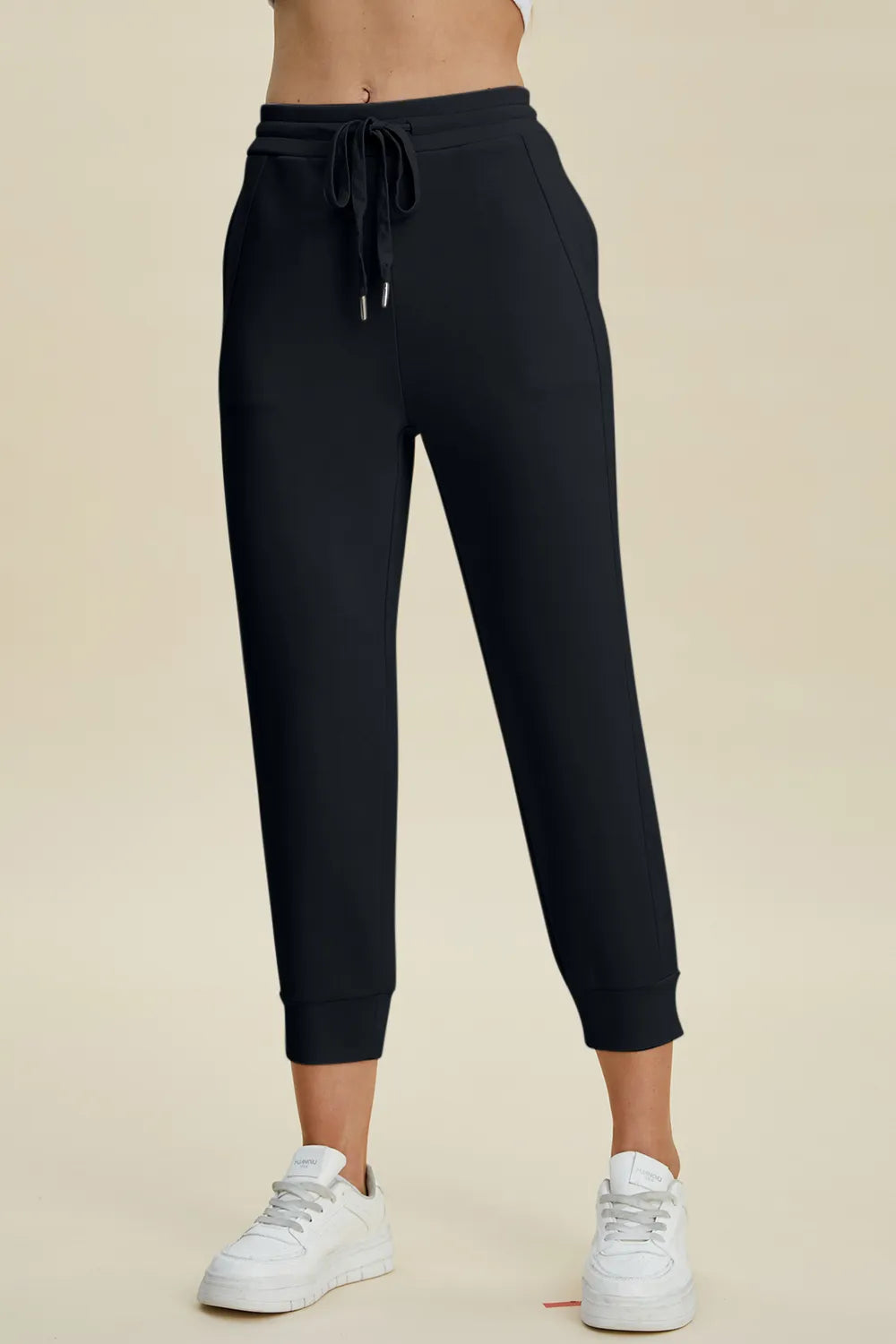 Black jogger pants worn by a person on a beige background