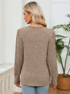 Woman wearing a brown ribbed sweater in a room with a plant and window.