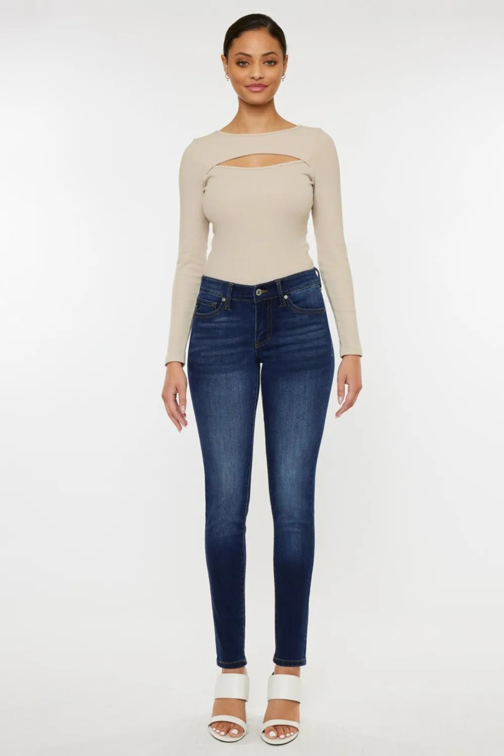 Woman wearing a beige long-sleeve top and blue jeans on a white background