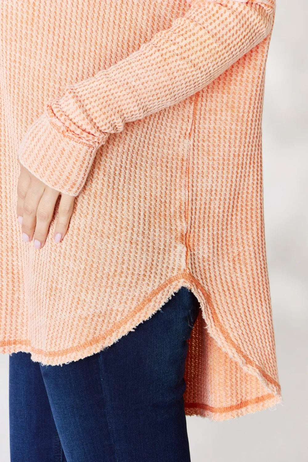 Person wearing a peach-colored knitted cardigan with a plain background