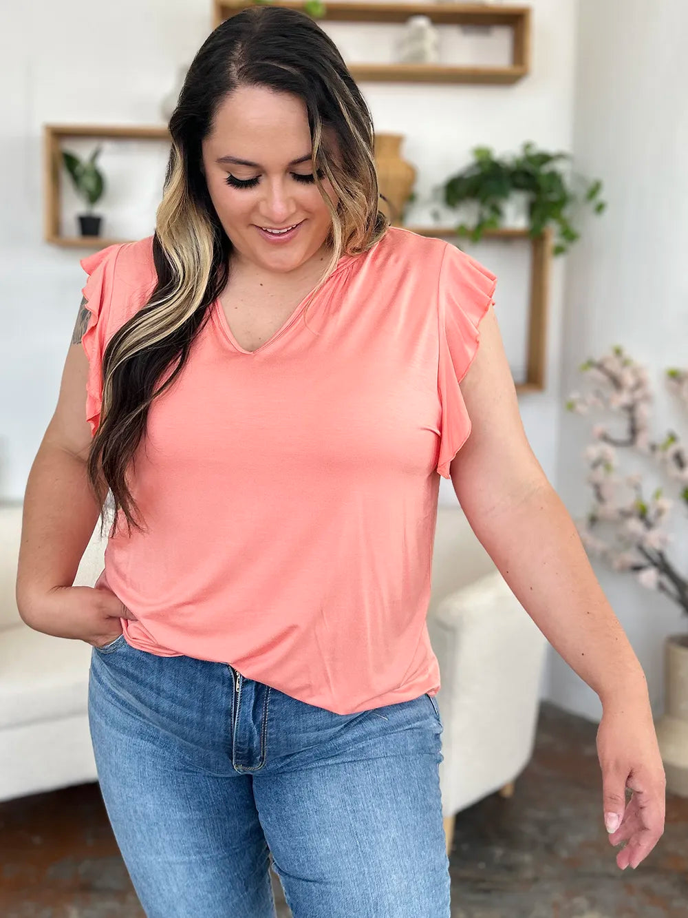 Woman wearing a pink sleeveless top and blue jeans in a living room setting.