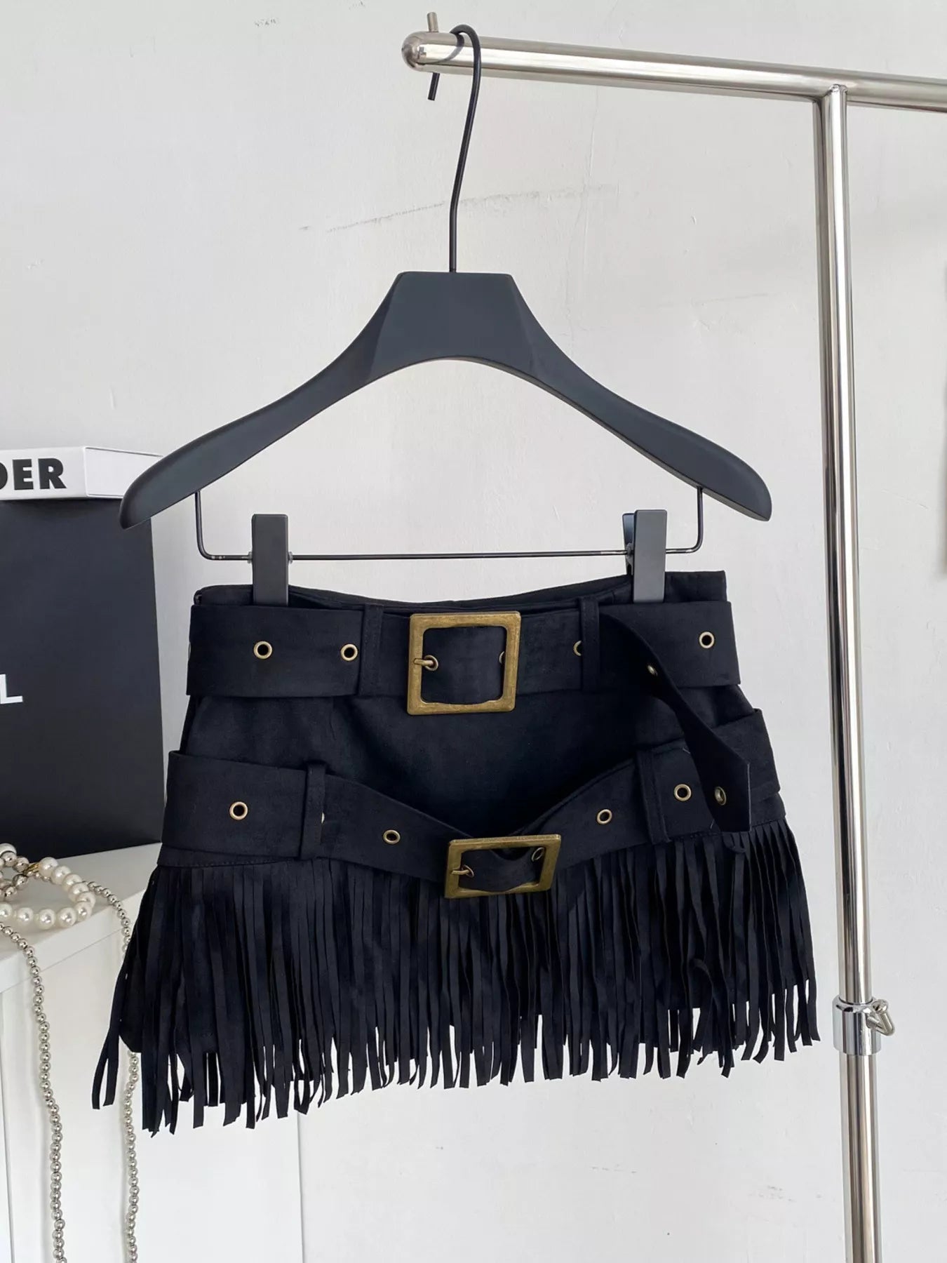 Black fringe skirt with gold buckles on a hanger against a white background